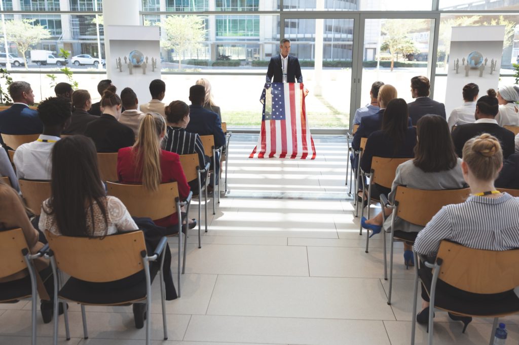 Mixed race man speaker speaking in a business seminar in office building with american flag